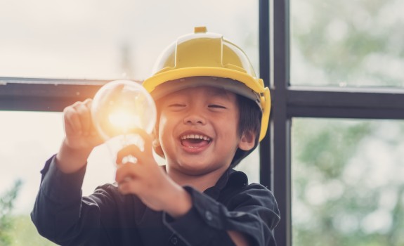 A child wearing a safety helmet holds a light bulb.