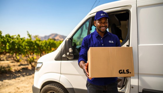 GLS driver holding a box in front of a GLS delivery vehicle parked in a vineyard