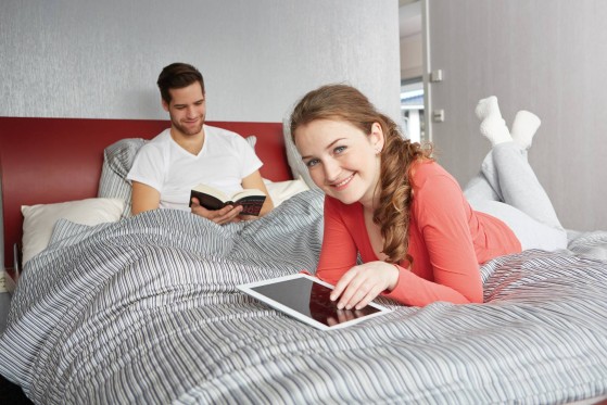 A man reading his book and a woman on her tablet in bed